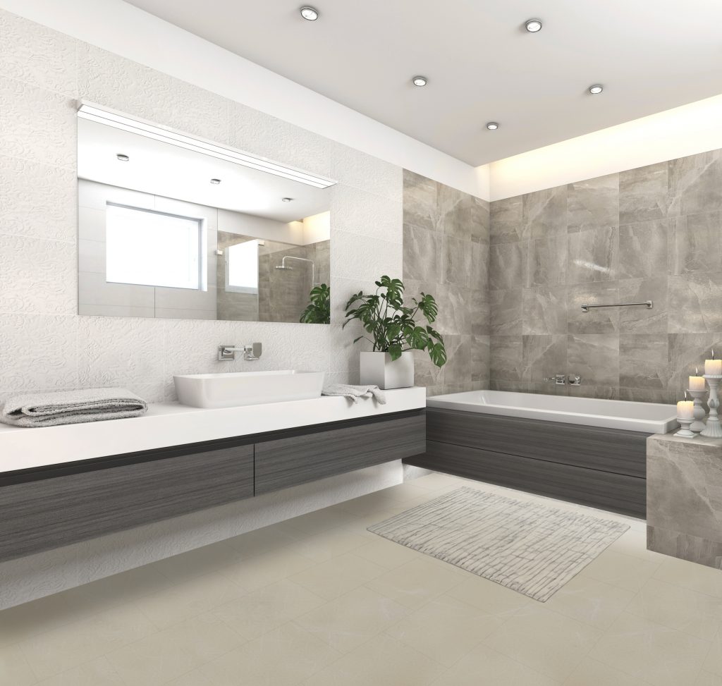 Luvanto Oyster Marble LVT flooring in a modern bathroom. The flooring has a light gray marble appearance with subtle veining. The bathroom features a white porcelain bathtub, a white porcelain sink with a dark wood vanity, and gray stone tile walls.